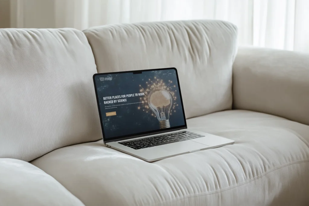 Laptop displaying the Institute of Management Psychology website on a cozy sofa, emphasizing workplace improvement through science.