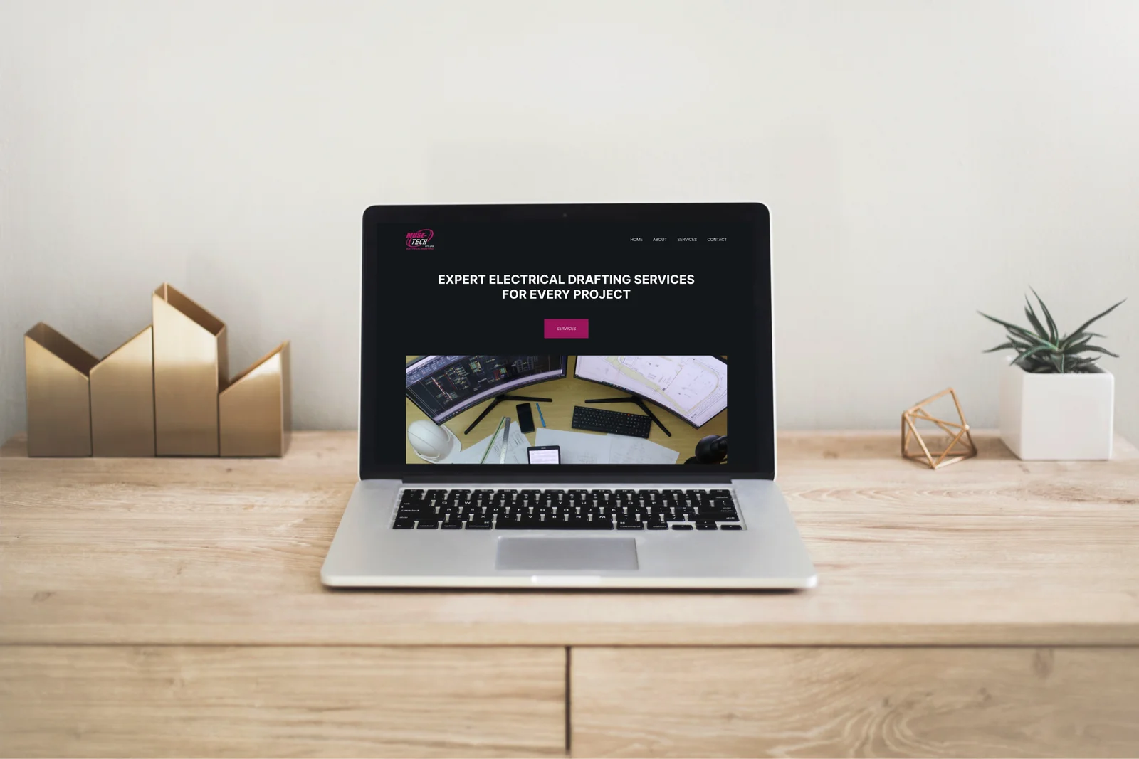 Laptop displaying a website for expert electrical drafting services, set on a wooden desk with decorative items.